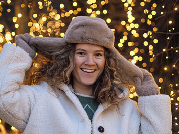 Portrait of young woman standing against illuminated christmas tree