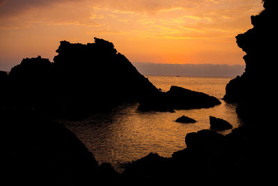 Silhouette rocks on sea against sky during sunset