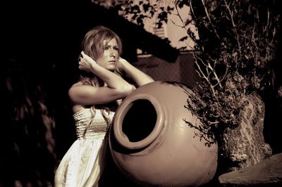 Young beautiful woman standing by clay pot in yard