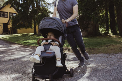 Midsection of father walking with male toddler in baby carriage on road