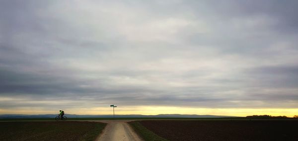 Road amidst field against sky during sunset