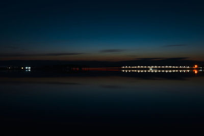 Illuminated city by sea against blue sky at night