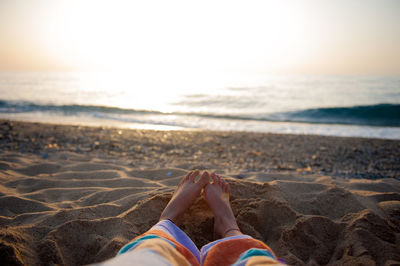 Low section of woman sitting on sand against sea at beach