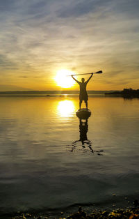 Silhouette man on paddleboard in lake against sky during sunset