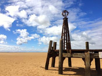 Rusty metallic beacon at beach against sky