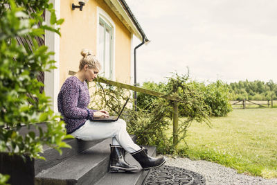Woman using laptop while sitting on steps outside house
