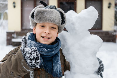 Portrait of smiling boy with snowman during winter