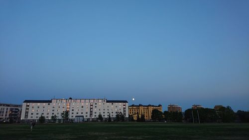 Buildings on lawn against clear blue sky