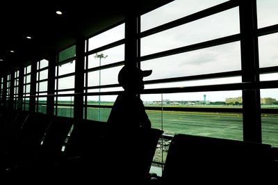 Silhouette person sitting at airport seen through glass window