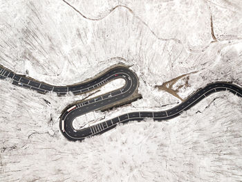 Curvy windy road in snow covered forest, top down aerial view.