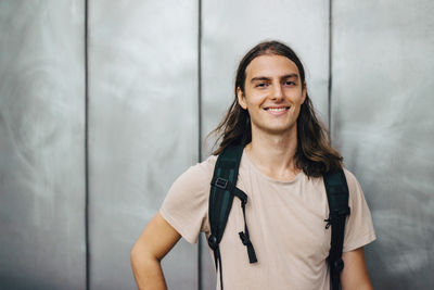 Portrait of a smiling young woman standing against wall