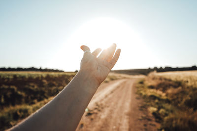 Midsection of person hand on field against sky