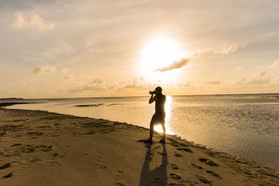 Shirtless man photographing through camera while standing on shore at beach