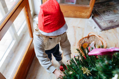 High angle view of little child in santa hat decorating christmas tree