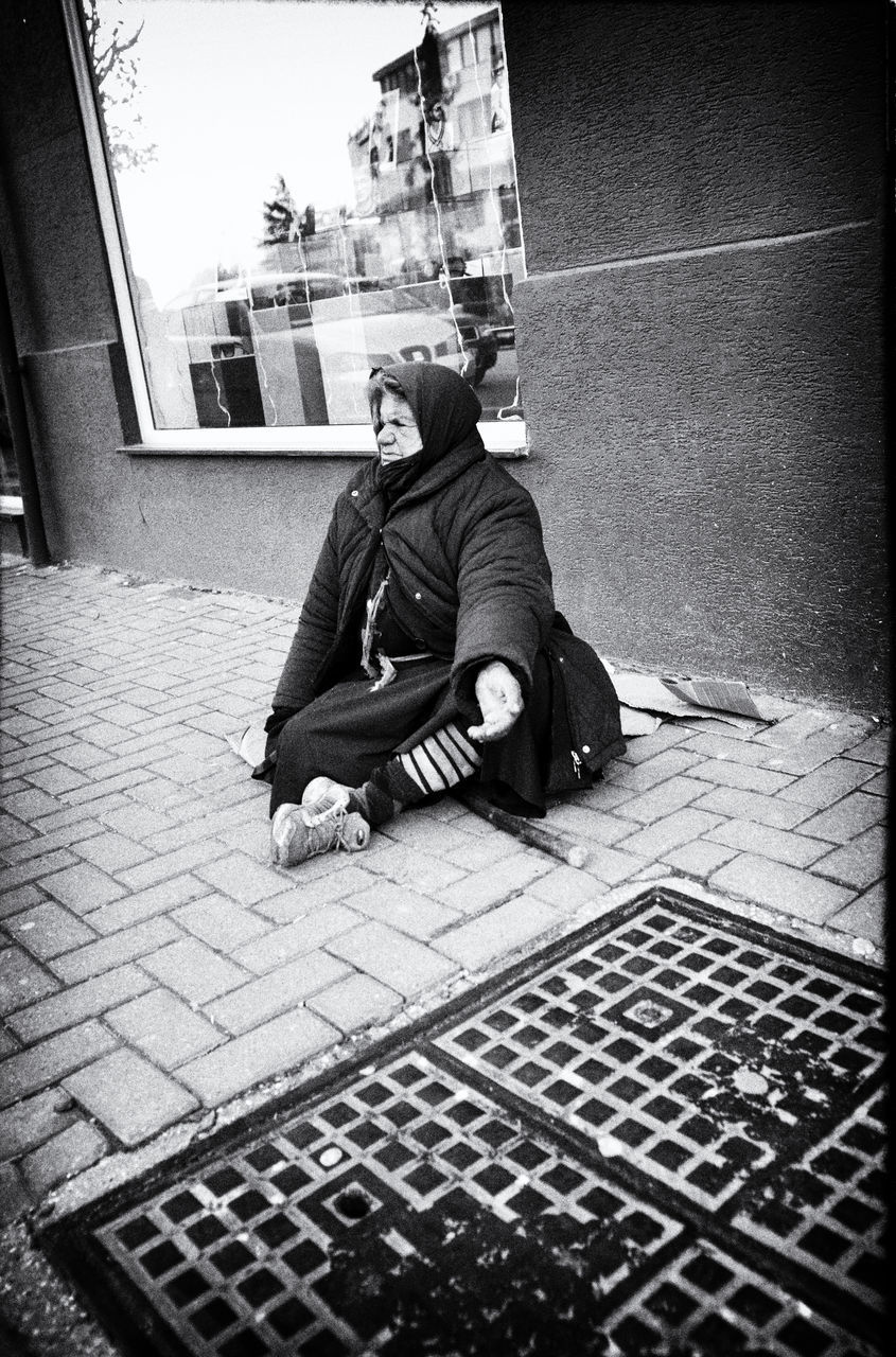 MAN SITTING ON SIDEWALK BY STREET
