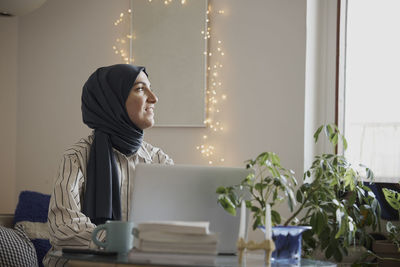 Contemplative female freelancer with laptop in living room while working from home