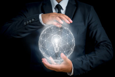 Midsection of man holding illuminated lighting equipment against black background