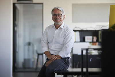 Smiling businessman sitting on table in office