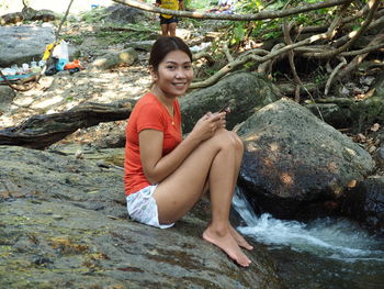Portrait of smiling young woman sitting on rock