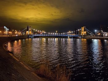 Illuminated bridge over river against sky in city at night