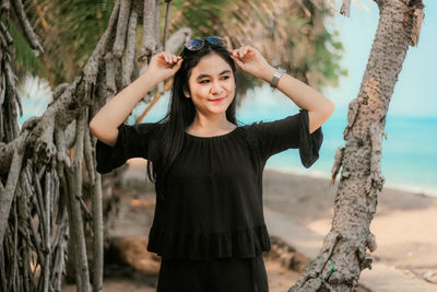 Portrait of smiling young woman standing on tree trunk