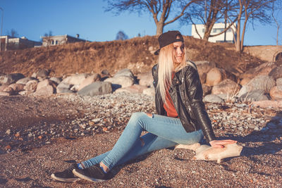 Portrait of smiling young woman sitting on rock against sky