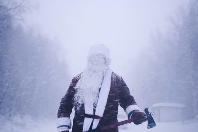 Mid adult man in santa costume standing in forest during winter
