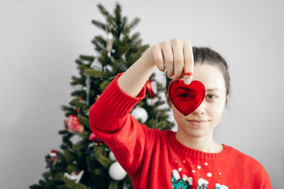 Portrait of woman holding heart shape by christmas tree at home
