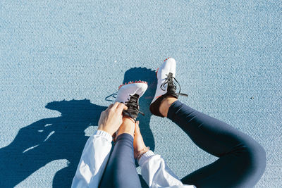 From above cropped unrecognizable female athlete in sportswear sitting on racetrack and changing footwear during track and field workout on sunny day on stadium