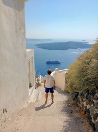 Rear view of man walking at coast village against clear sky and scenic view of sea and caldera