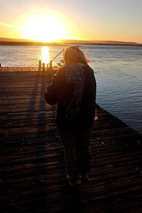 Rear view of woman standing at sea shore during sunset