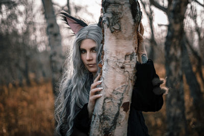 Portrait of young woman with tree trunk in forest