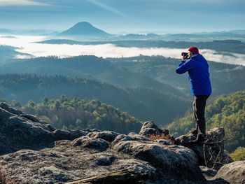 Man photographing on rock against mountains