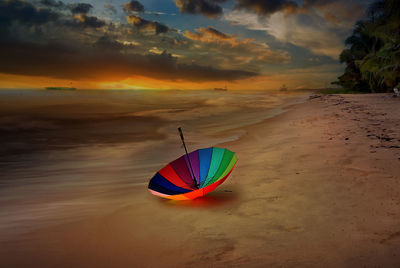 Multi colored umbrellas on beach against sky during sunset