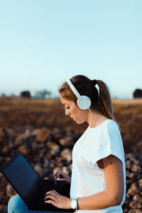 Young woman using laptop on land against sky