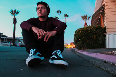 Young man sitting on tree against sky