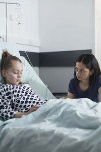 Worried woman looking at daughter with oxygen tube in hospital ward