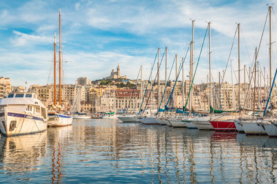 Sailboats moored in harbor against sky in city