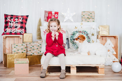  little girl at home with jack russell dog. kid wearing red christmas dress at home.christmas deco