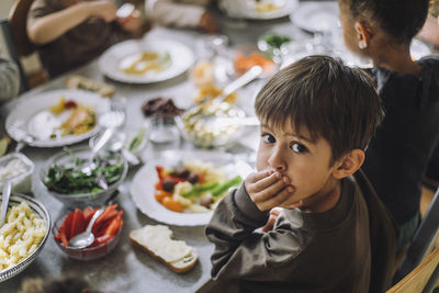 Portrait of boy covering mouth with hand with breakfast on table at day care center