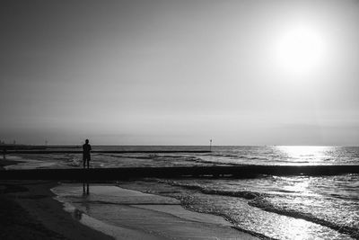 Silhouette man standing on shore at beach against clear sky