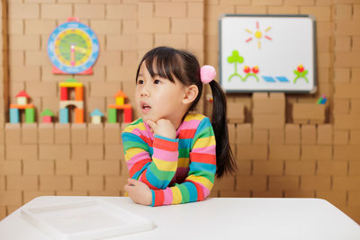 Portrait of young girl sitting on chair against carton block wall background 