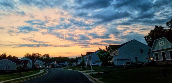 Road by buildings against sky during sunset