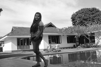 Portrait of woman standing by swimming pool against sky