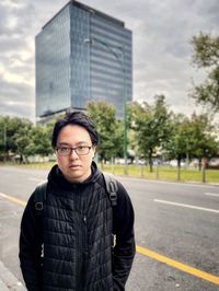 Portrait of young asian man standing beside road against building in the city.