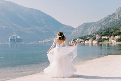 Rear view of bride standing at beach against mountains and sky
