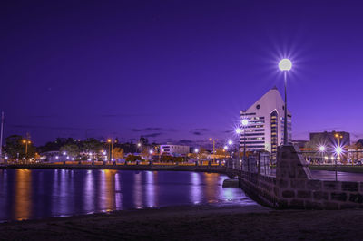 Illuminated buildings by river against sky at night