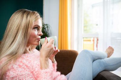 A young woman drinks coffee while sitting in the living room.