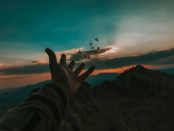 Cropped hand of person against sky during sunset