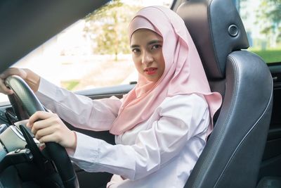 Portrait of young woman in hijab driving car